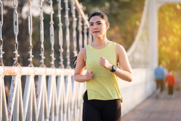 Een jonge Aziatische vrouw atleet atleet in sportoutfit joggen en trainen in het stadspark in de ochtend. Gezonde levensstijl jonge sportieve Aziatische vrouw die in tropisch park loopt. Sport en recreatie