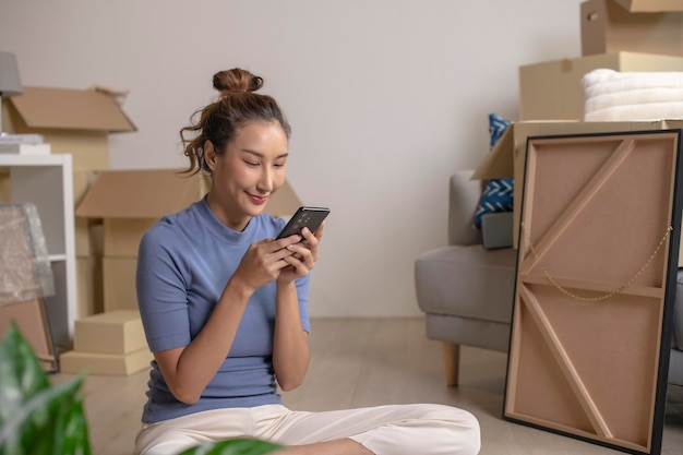 Foto een jonge aziatische vrouw die in een nieuw huis zit en een smartphone gebruikt nadat ze is ingetrokken