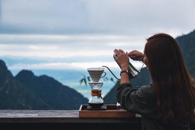 Een jonge aziatische vrouw die infuuskoffie maakt met een prachtige berg- en natuurachtergrond