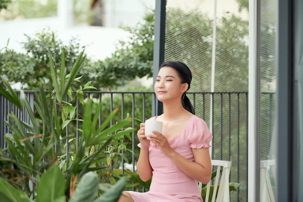 Een jonge Aziatische vrouw drinkt koffie op het balkon