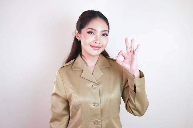 Een jonge Aziatische vrouw in bruin kaki uniform met duimen omhoog of OK teken Indonesische overheidsmedewerker