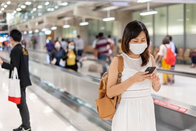 Een jonge Aziatische vrouw met een masker op de luchthaven is op weg naar het vliegtuig bij de gate. Reizen tijdens de COVIT-19-epidemie