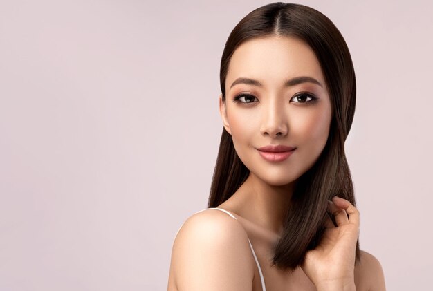 Een jonge Aziatische vrouw met zwarte ogen toont een goed verzorgde zachte huid en delicate make-up op het gezicht.
