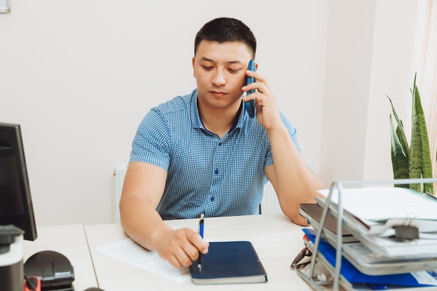 Een jonge Aziatische zakenman praat aan de telefoon om werk op kantoor te bespreken, de man is Aziatisch