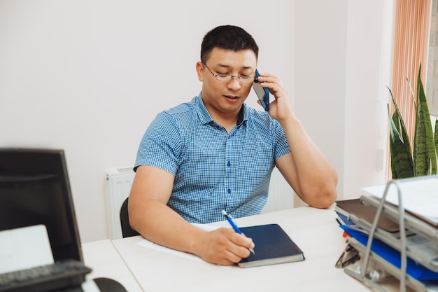 Een jonge Aziatische zakenman praat aan de telefoon om werk op kantoor te bespreken, de man is Aziatisch