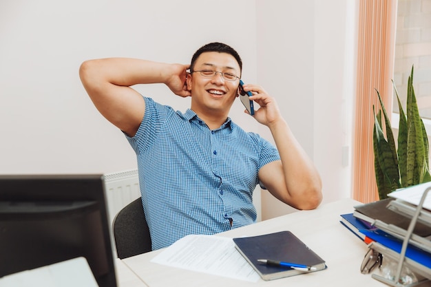 Een jonge Aziatische zakenman praat aan de telefoon om werk op kantoor te bespreken, de man is Aziatisch