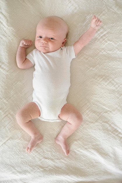 Een jonge baby liggend op zijn rug op een bed, armen en benen strekken zich uit