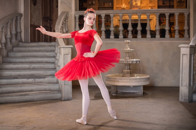 Een jonge ballerina in een rode tutu danst tegen het theatrale decor van het paleis.