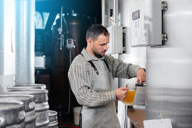 Een jonge, bebaarde brouwer voert de kwaliteitscontrole uit van vers gebrouwen bier in de brouwerij.