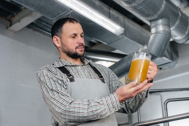 Een jonge, bebaarde brouwer voert de kwaliteitscontrole uit van vers gebrouwen bier in de brouwerij.