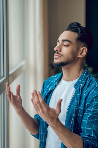 Een jonge, bebaarde man die bidt met zijn ogen dicht