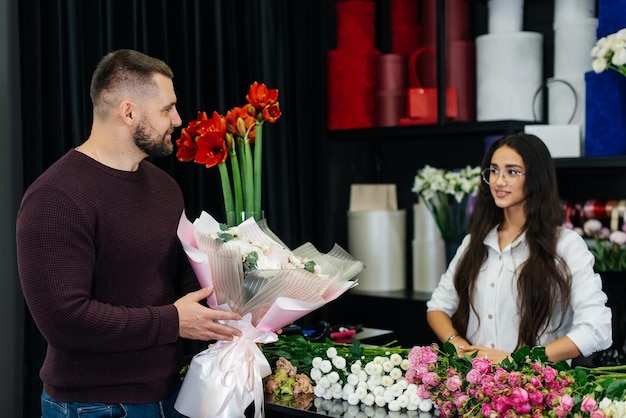 Een jonge, bebaarde man koopt een mooi boeket bloemen voor de vakantie van een meisje in een gezellige bloemenwinkel Bloemisten en boeketten maken in een bloemenwinkel Klein bedrijf