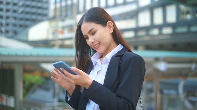 Een jonge bedrijfsvrouw die zwart kostuum draagt, gebruikt slimme telefoon, in de stad, Business Lifestyle Concept.