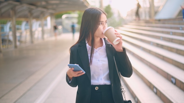 Een jonge bedrijfsvrouw die zwart kostuum draagt, gebruikt slimme telefoon