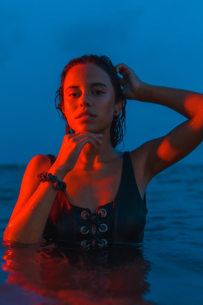 Een jonge blanke brunette die 's nachts in de zee baadt met een verlicht rood licht