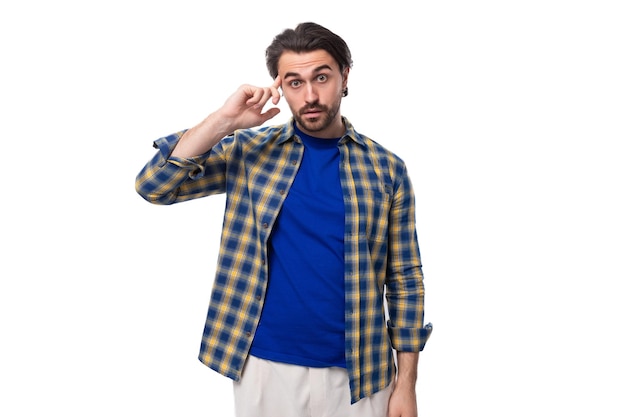Een jonge blanke brunette man met een baard en een oorbel is gekleed in een blauw geruite shirt en
