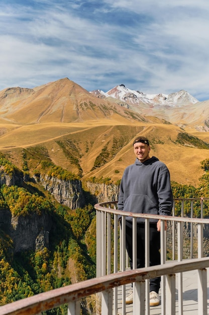 Een jonge blanke man staat op een observatiedek reist door het herfstlandschap van de bergen in de kloof van de kaukasus, georgië verticale framebanner of ansichtkaartidee met plaats voor tekst