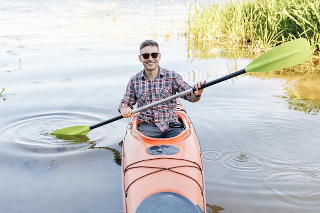 Een jonge blanke man zit in een kajak en peddelt Het concept van waterentertainment