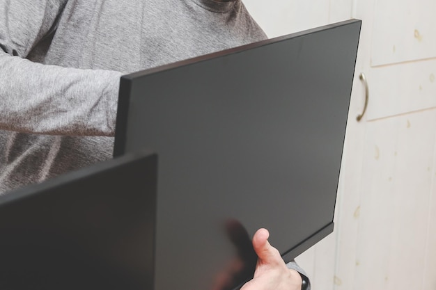 Een jonge blanke man zonder gezicht houdt een computermonitor vast met zijn handen