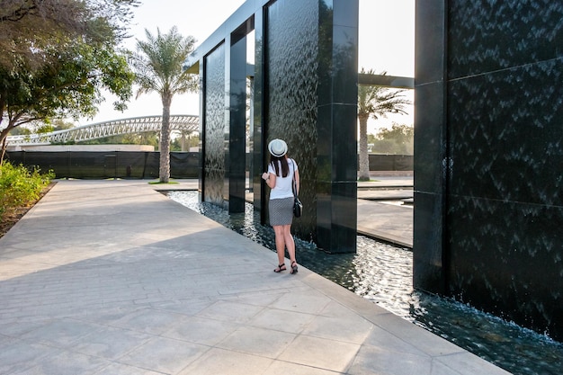 Een jonge blanke meisjestoerist met een witte hoed loopt in een stadspark met exotische palmbomen in Abu Dhabi, VAE