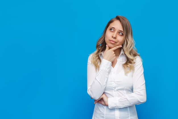 Een jonge blanke, mooie blonde vrouw in een wit overhemd overweegt wonderen, denkt dat ze opkijkt