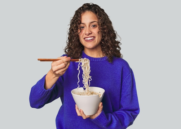 Een jonge blanke vrouw die noddles eet met stokjes, erg blij