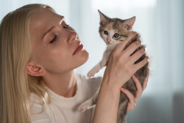 Een jonge blonde vrouw houdt een klein katje in haar armen voor haar gezicht en kijkt met liefde naar het huisdier. De vreugde die dieren in huis brengen.