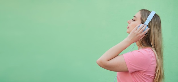 Een jonge blonde vrouw in een roze shirt luistert naar muziek in een blauwe koptelefoon die haar ogen bedekt tegen haar