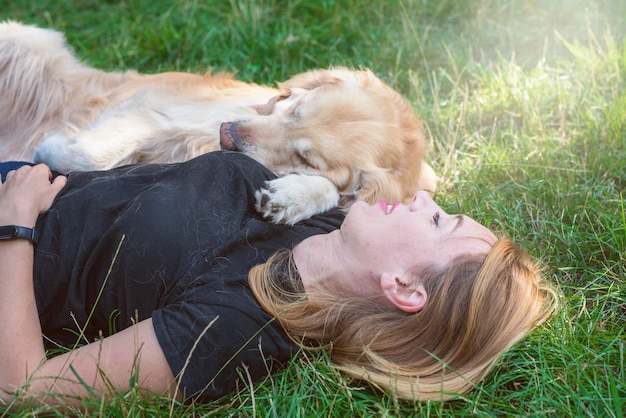 Een jonge blonde vrouw ligt op het gras met haar hond. hondenras retriever met een meisje in het park.