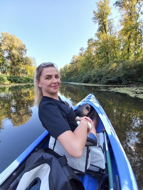 Een jonge blonde vrouw zwemt in een boot en kijkt terug met een glimlach. Toerisme, sport en recreatie in de buitenlucht.