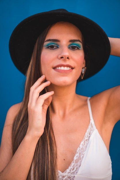 Een jonge brunette met een zwarte hoed en een wit t-shirt op een blauwe achtergrond