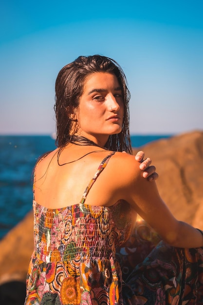 Een jonge brunette met nat haar en een gebloemde jurk aan zee, zomerse levensstijl