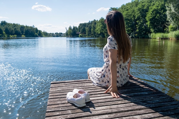 Een jonge brunette vrouw, gekleed in witte jurk zittend op een houten platform op het meer