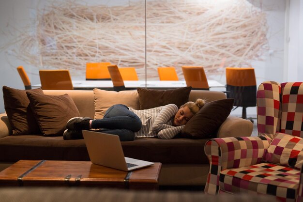 Een jonge casual zakenvrouw die op een bank slaapt tijdens een werkpauze in een creatief kantoor