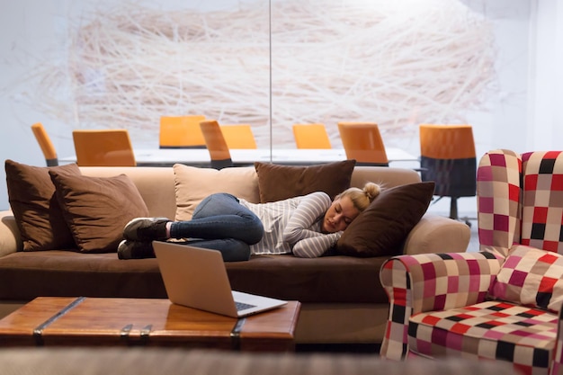 Een jonge casual zakenvrouw die op een bank slaapt tijdens een werkpauze in een creatief kantoor