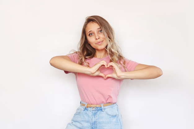 Een jonge charmante blonde vrouw die een hartvorm vormt met haar handen geïsoleerd op een witte achtergrond