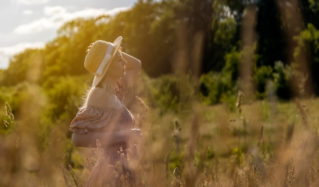 Een jonge charmante vrouw in een jurk en een strohoed poseert bij zonsondergang op een weide Vrouw in focus