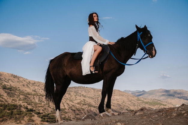 Een jonge dame ruiter in een witte jurk zit in het zadel op een paard, tegen de achtergrond van een prachtig berglandschap. Het concept van romantiek, sprookjes. Voorbeeld van een afgewerkte boekomslag