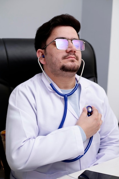 Foto een jonge dokter zit in de kliniek en controleert zijn hartslag met een stethoscoop