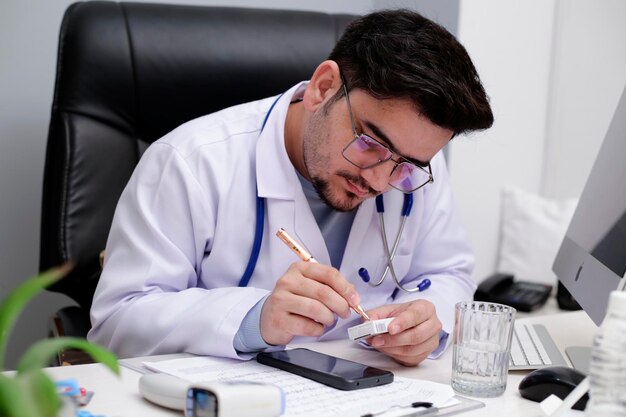 Foto een jonge dokter zit in de kliniek met een pen in de hand en schrijft iets op de medicijndoos