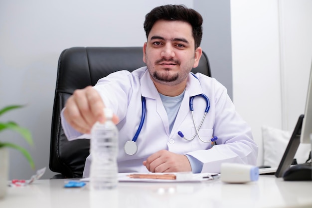 Een jonge dokter zit op de stoel in de kliniek en houdt een waterfles in de hand