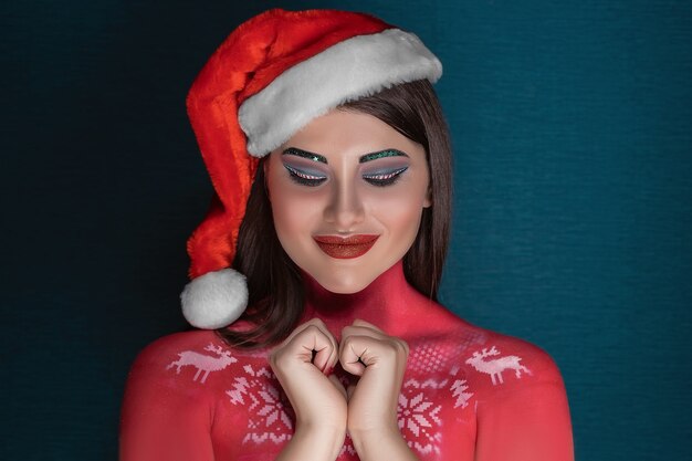 Een jonge donkerbruine vrouw met ideale art-make-up en in een kerstmuts doet een wens met gesloten ogen