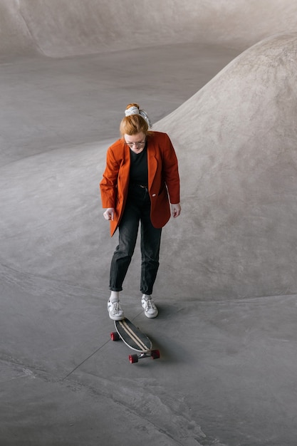 Een jonge en mooie vrouwelijke skater, een vrouw in een oranje jasje, rijdt op een skateboard op een skatepad