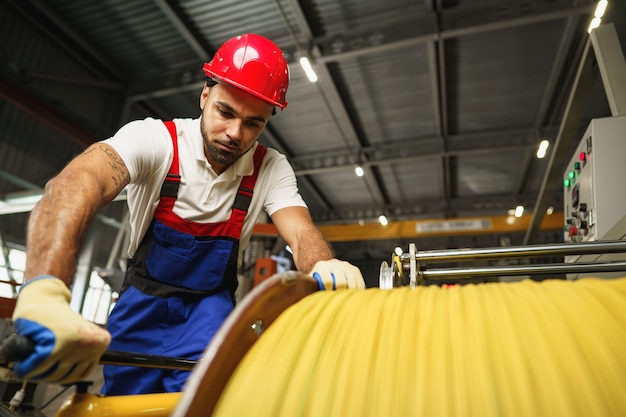 Een jonge fabrieksarbeider rolt een zware rol elektrische kabel