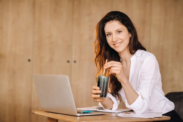 Een jonge freelance vrouw met een cocktail in haar handen op haar werkplek op het werk