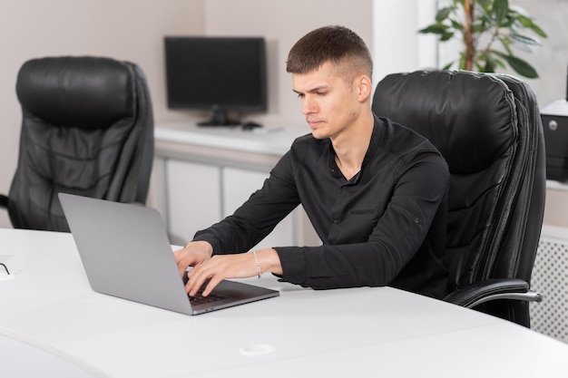 Een jonge freelancer met een wit overhemd gebruikt een laptop terwijl hij op kantoor zit