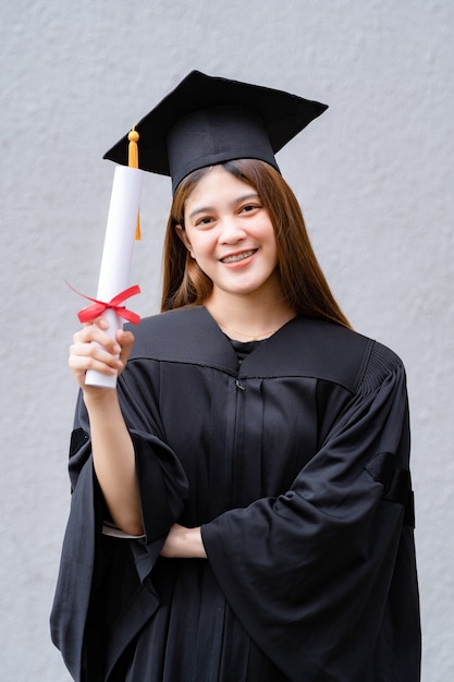 Een jonge, gelukkige aziatische vrouw afgestudeerd aan de universiteit in afstudeerjurk en baret heeft een diploma en viert onderwijsprestaties op de universiteitscampus. onderwijs stockfoto's