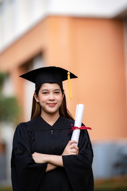 Een jonge, gelukkige Aziatische vrouw afgestudeerd aan de universiteit in afstudeerjurk en baret heeft een diploma en viert onderwijsprestaties op de universiteitscampus. Onderwijs stockfoto's