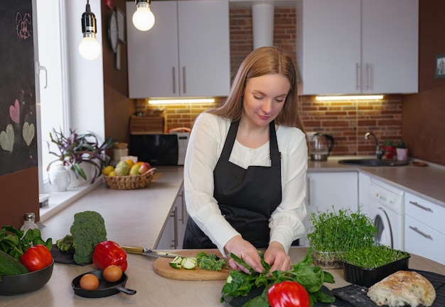 Een jonge gelukkige dame die in de keuken staat tijdens het koken