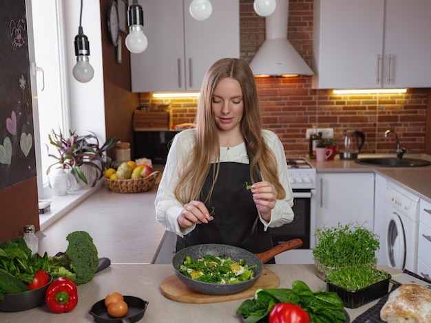 Een jonge gelukkige dame die in de keuken staat tijdens het koken